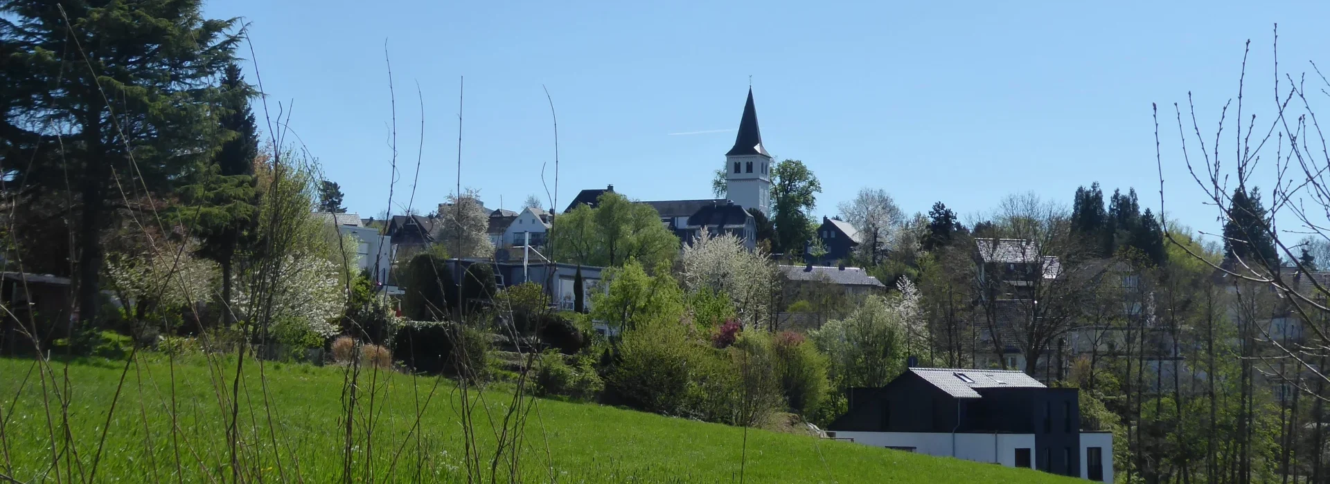 Blick vom Breitenweg auf Herkenrath mit Wohnhäusern, Gärten und St. Antonius Abbas, April 2022